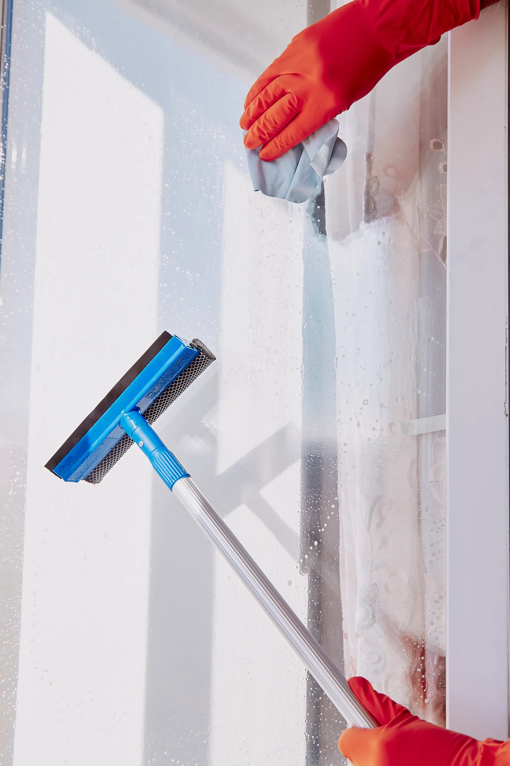 Person using microfiber cloth and squeegee during window cleaning. 